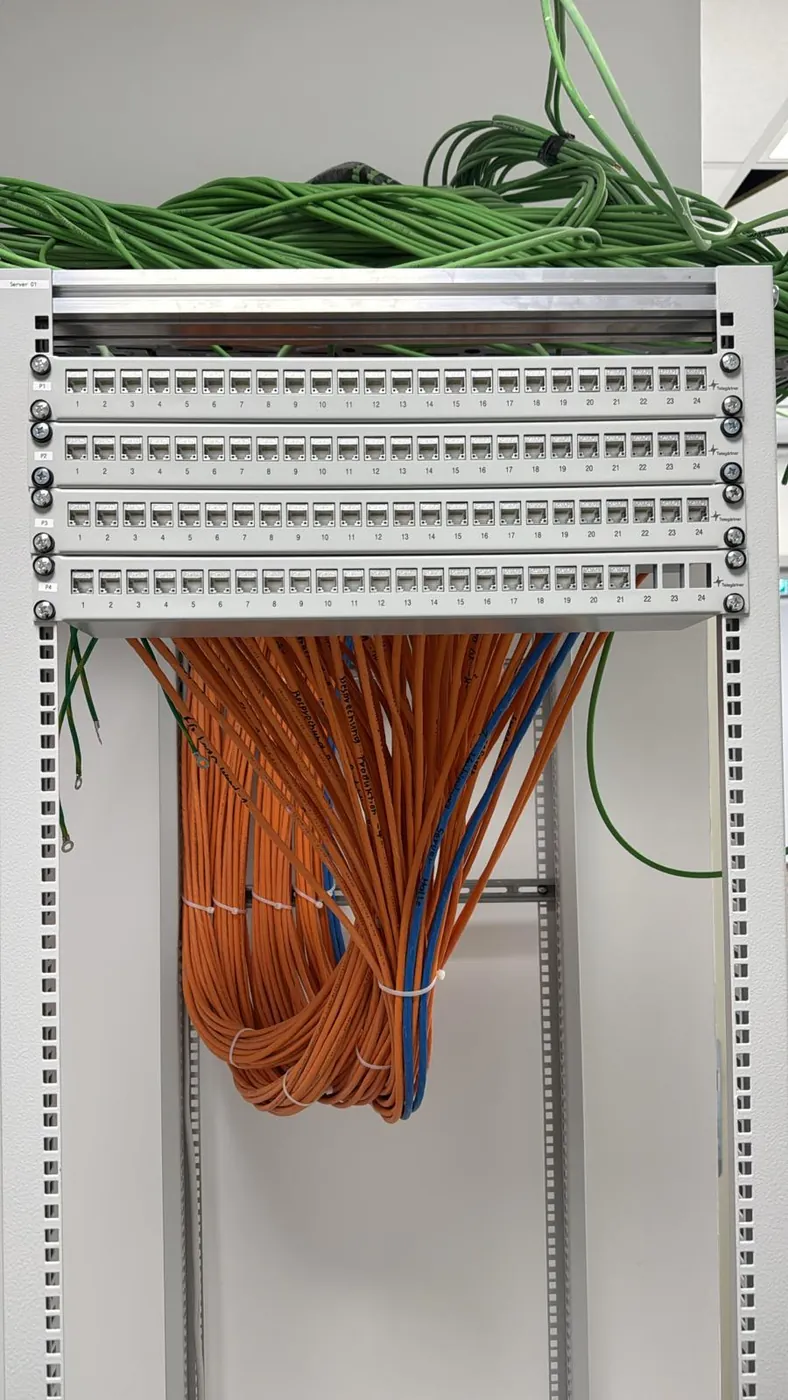 Vier aufgelegte Patchfelder in einem Serverschrank, darüber gebündelte Verlegekabel in der Kabeltrasse